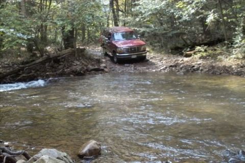 1994 Ford Bronco - Ford Bronco navigating a stream in a forest setting.