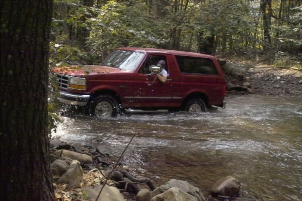 Red 1994 Ford Bronco driving through a stream