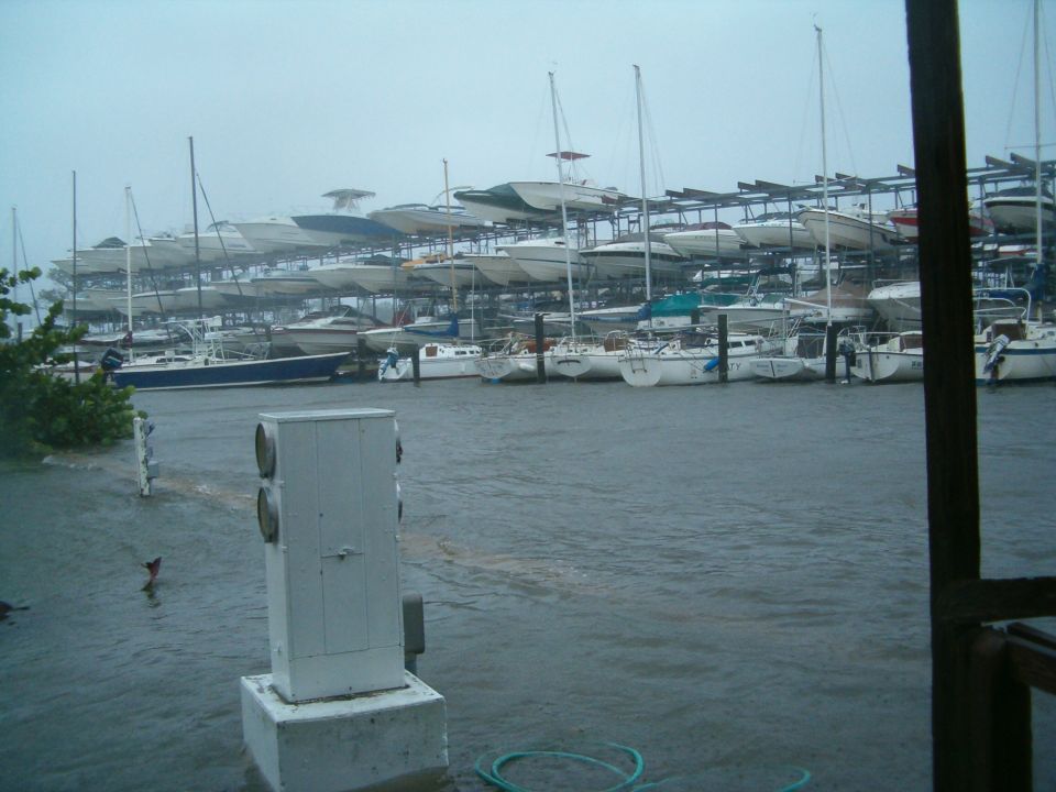 Many boats are stored on racks in a marina with choppy water, suggesting stormy weather