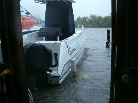 1991 Ford Bronco - A white boat with a black canopy and stern cover is docked in choppy water, with trees visible in the background.