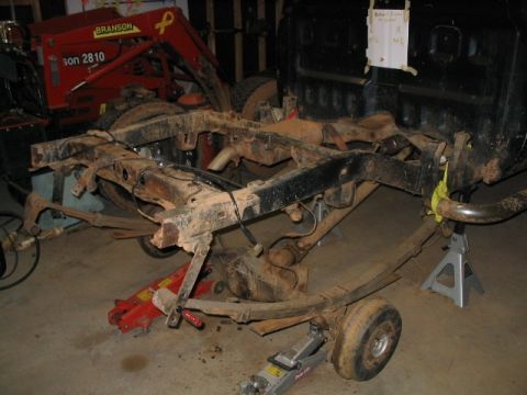 1986 Ford F-150 - The chassis of a truck is disassembled and supported by jack stands in a garage.