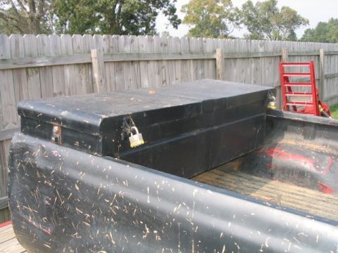 1986 Ford F-150 - A black toolbox sits secured in the bed of a truck, with a wooden fence in the background.