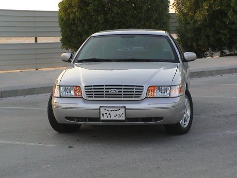 2004 Ford Crown Victoria - A silver 2004 Ford Crown Victoria is shown from the front, displaying its grille and headlights. The vehicle has a Saudi Arabian license pl…