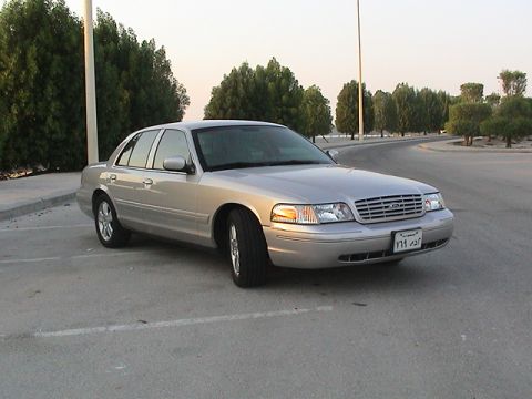 2004 Ford Crown Victoria - A silver 2004 Ford Crown Victoria sedan is parked outdoors near trees and water.