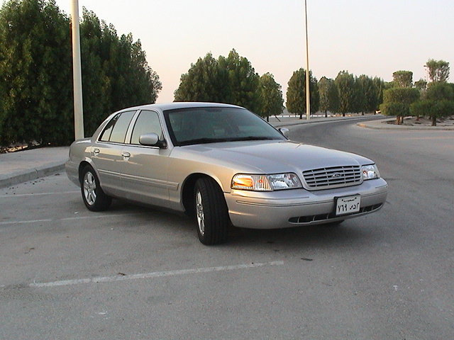 Silver 2004 Ford Crown Victoria parked on asphalt with trees and a body of water in the background