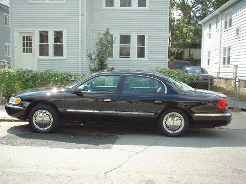 1997 Ford Crown Victoria - Black Lincoln Continental parked on street with houses in background.
