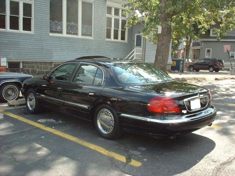 1997 Ford Crown Victoria - A black Lincoln Continental sedan is parked in a lot next to a building, with another vehicle visible in the background.