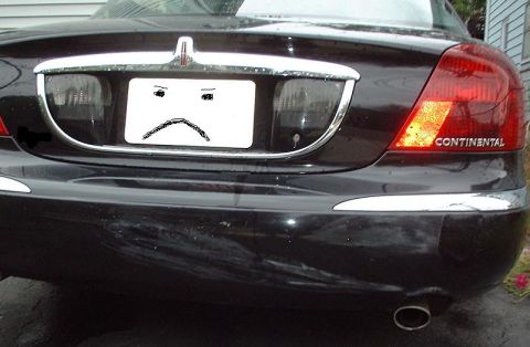 1997 Ford Crown Victoria - The rear of a Lincoln Continental shows a sad face drawn on its license plate and some damage to the bumper.