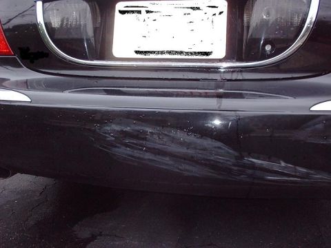 1997 Ford Crown Victoria - Rear bumper of a black car shows extensive scuff marks and damage.