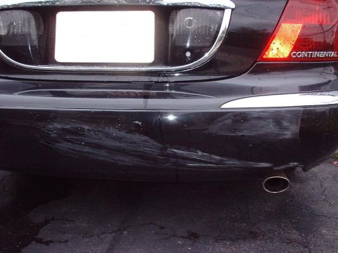1997 Ford Crown Victoria - Rear view of a black car showing a damaged bumper and a 'CONTINENTAL' badge on the taillight.