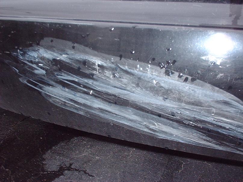 Close-up of a black car bumper with white paint transfer and deep scratches