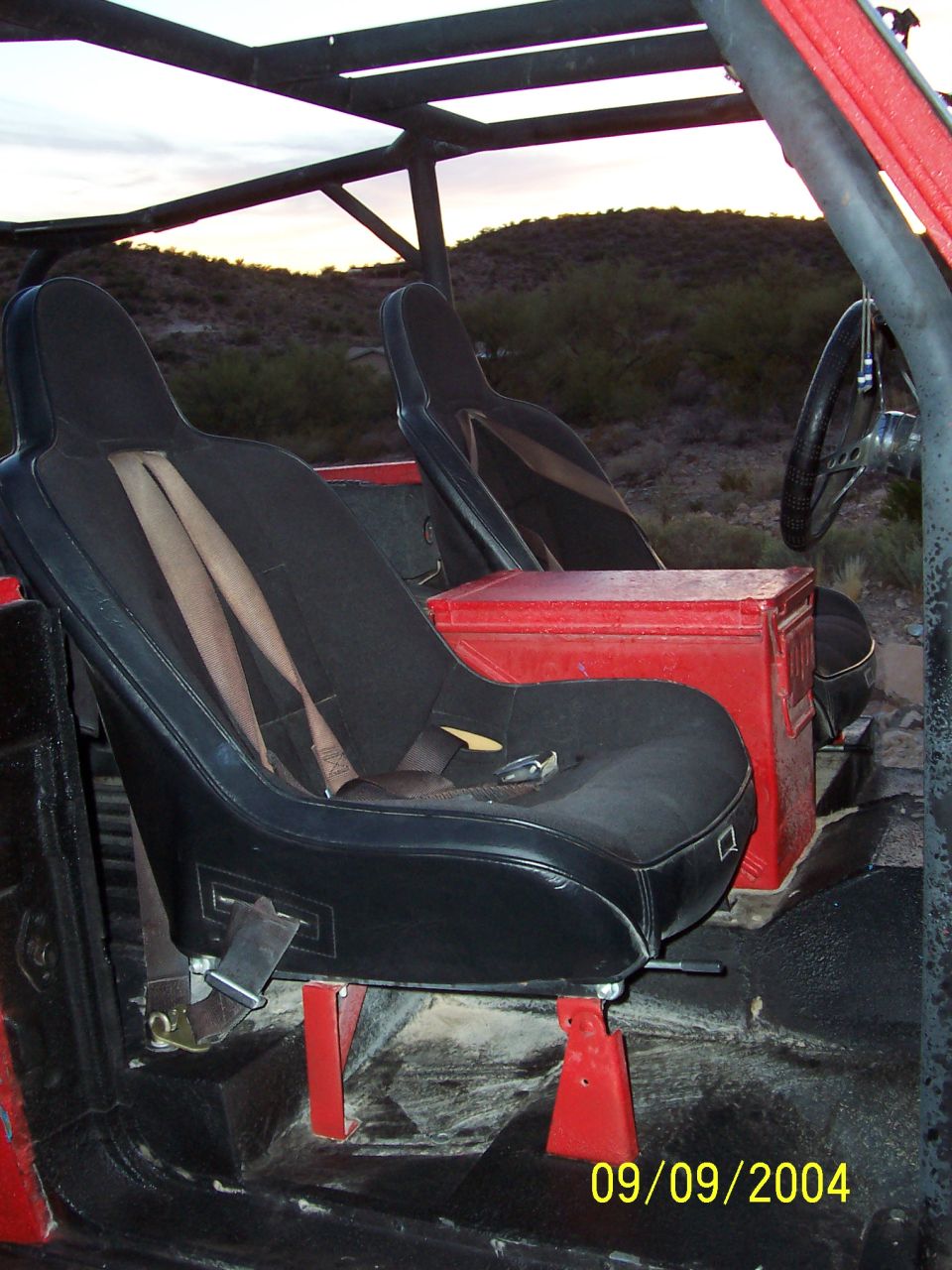 Black bucket seats and red ammo can inside open-top off-road vehicle in desert