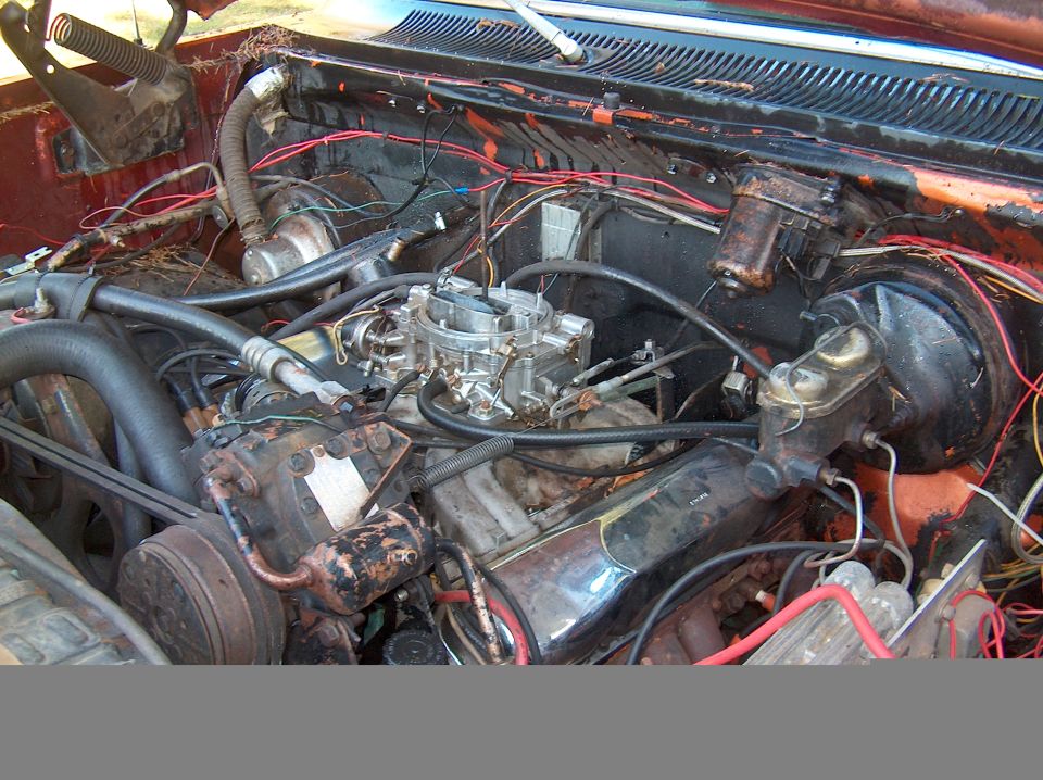 V8 engine bay with chrome carburetor, rusty brackets and tangled wiring in a Dodge truck
