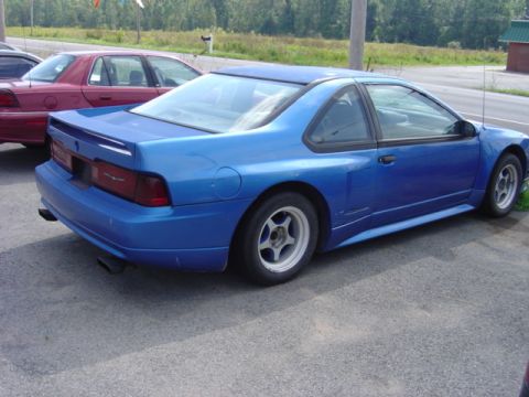 1998 Ford Taurus - A blue coupe is parked next to a red sedan. The blue car has a spoiler and aftermarket wheels.