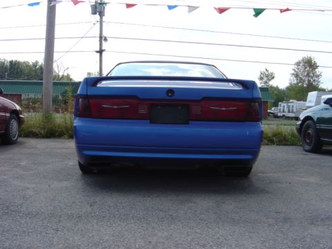 1998 Ford Taurus - A blue coupe with a spoiler is parked outside, with other vehicles nearby.