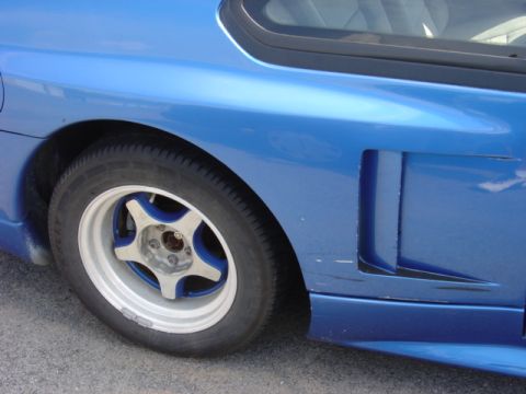 1998 Ford Taurus - Close-up of a blue car's rear side panel and wheel, showing custom rims.