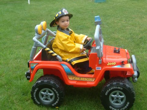 1989 Ford Bronco - A young child dressed as a firefighter sits in a toy Jeep, ready for adventure.