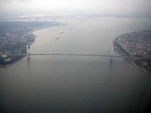 1995 Ford Bronco - An aerial perspective captures a large suspension bridge connecting two landmasses, with several cargo ships navigating the waterway below.