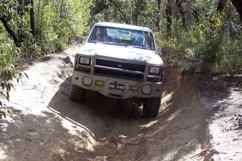 1982 Ford Bronco - This white off-road vehicle, identified by license plate RB 045, navigates a challenging dirt track through a wooded area.
