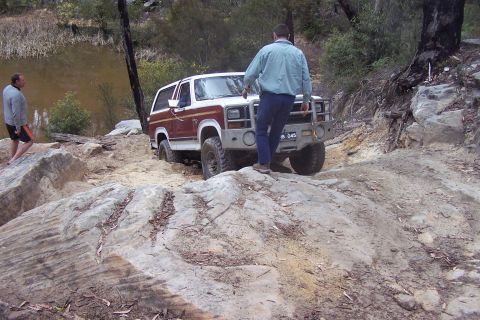 1982 Ford Bronco - A man walks near a Ford Bronco as it drives over rocks.