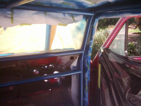 1978 Ford Bronco - The interior of a vehicle is being prepped for painting, with a blue roll cage and taped-off windows.