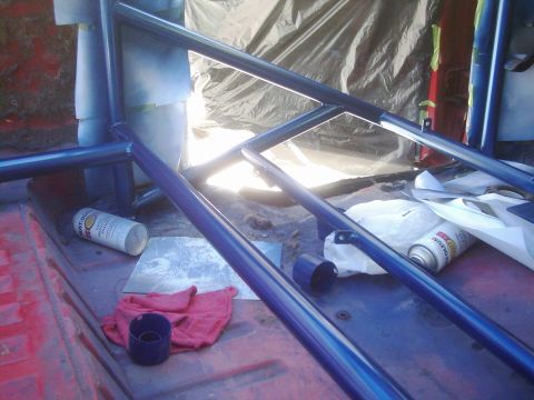 1978 Ford Bronco - Roll cage being painted blue inside a vehicle, with spray paint cans and rags on the floor.