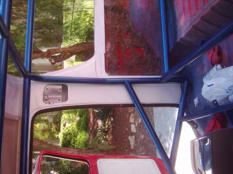 1978 Ford Bronco - The interior of a vehicle is shown with a blue roll cage installed, and red interior panels visible.