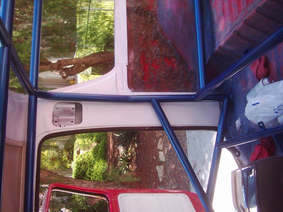 Inside of a vehicle with a blue roll cage. Red interior visible. Trees and greenery outside