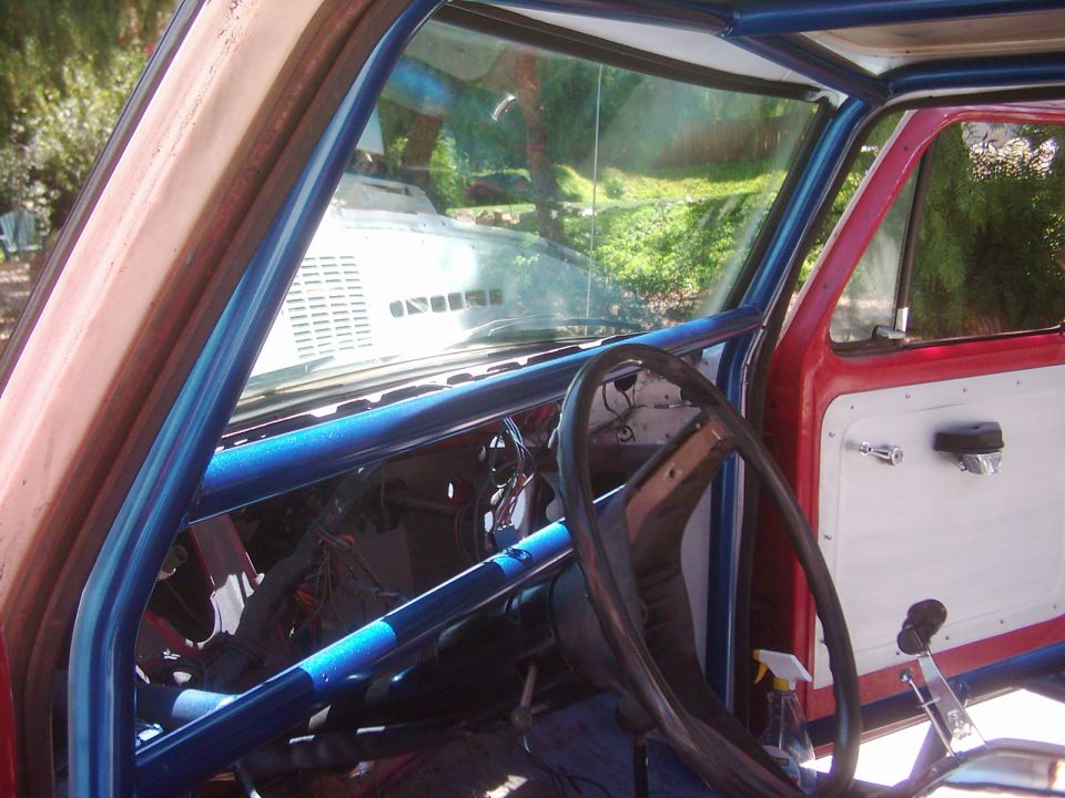 1978 Ford Bronco interior with blue roll cage, red exterior paint, and white door panel