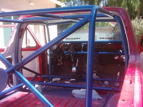 1978 Ford Bronco - The interior of a 1978 Ford Bronco shows a blue roll cage installed over the red bed and interior.