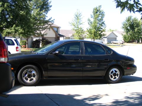 1996 Ford Taurus - A black sedan is parked in a suburban driveway next to a white SUV.