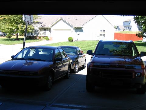 1996 Ford Taurus - Three vehicles are parked in a garage, with a suburban house and yard visible beyond the background.