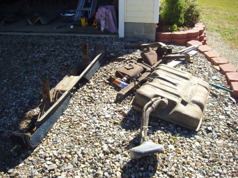 Ford F-250 fuel tank and bumper on gravel. Other parts are scattered nearby