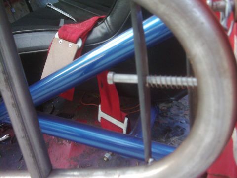 1978 Ford Bronco - Close-up view of a vehicle's interior, showing a roll cage and racing seat with a red seatbelt.