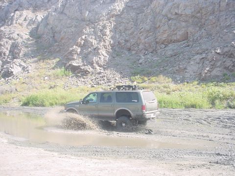 1988 Ford Bronco - A green SUV navigates a muddy terrain, kicking up water and dirt.