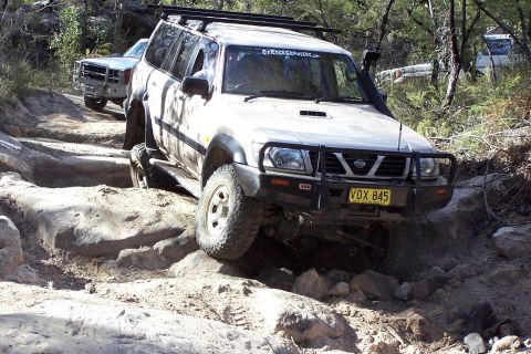 1982 Ford Bronco - Nissan Patrol tackling a challenging rocky path, with a second vehicle following.