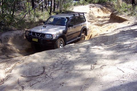 1982 Ford Bronco - Nissan Patrol tackling an off-road course with steep inclines and sandy terrain.