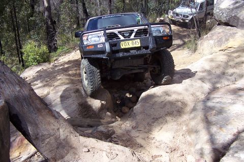 1982 Ford Bronco - Two off-road vehicles navigate a challenging rocky terrain in a wooded area.