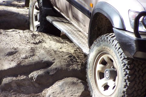 1982 Ford Bronco - This SUV is navigating a sandy and rocky path, with its front wheel and diamond plate running board clearly visible.