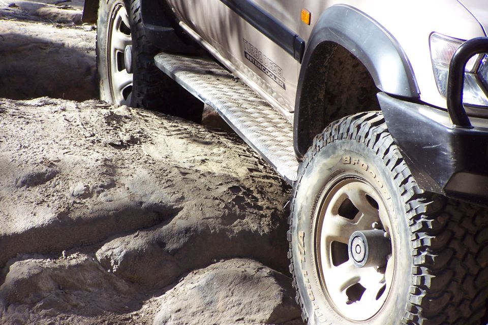 Tan SUV front wheel and running board on sandy terrain