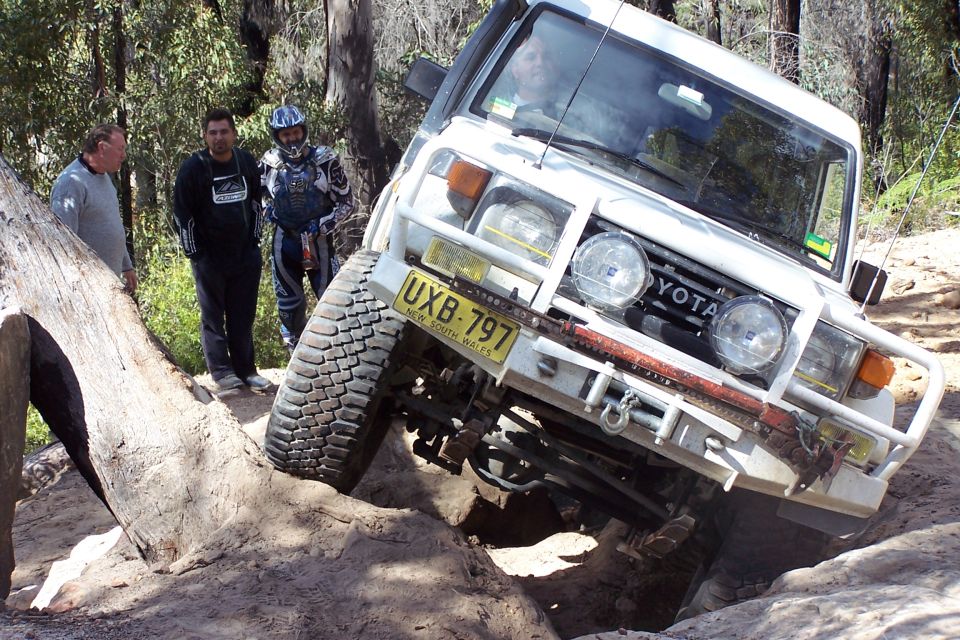 White Toyota 4x4 with bull bar and plate UXB-797 flexing over rocks on a bush trail as onlookers watch