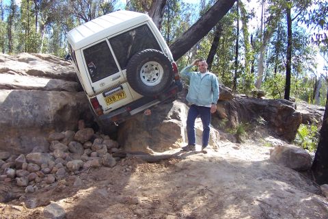 1982 Ford Bronco - A man poses next to his Toyota Land Cruiser as it navigates a difficult rocky off-road obstacle.