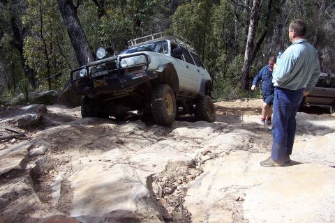 1982 Ford Bronco - An off-road SUV navigates a challenging rocky path, with two people observing the action.