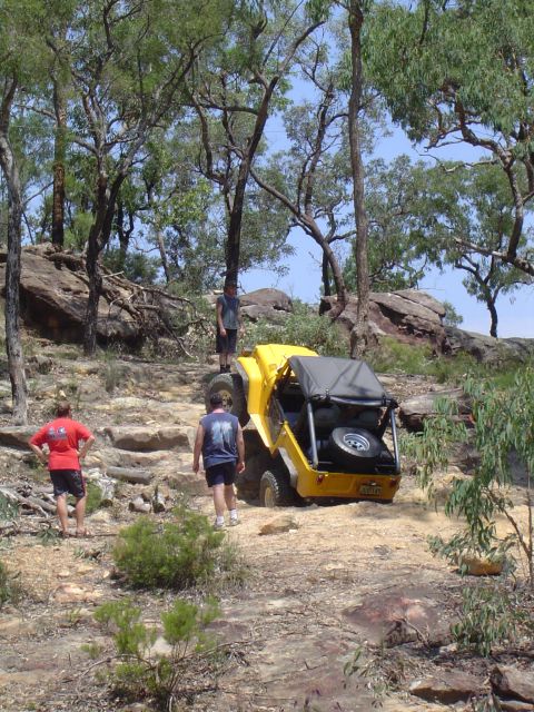 1982 Ford Bronco - A yellow off-road vehicle navigates a steep, rocky terrain with onlookers observing the challenging climb.