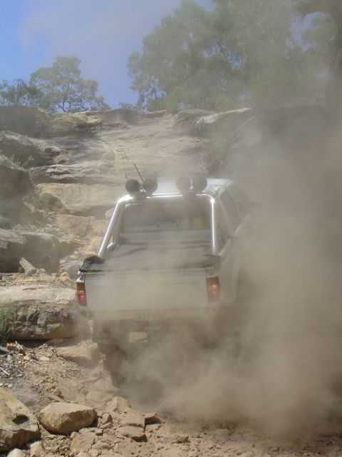 1982 Ford Bronco - This off-road vehicle navigates a challenging rocky incline, enveloped in a cloud of dust.