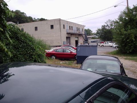 1998 Ford Taurus - A red 1998 Ford Taurus is parked next to a large dumpster in a lot beside a brick building.