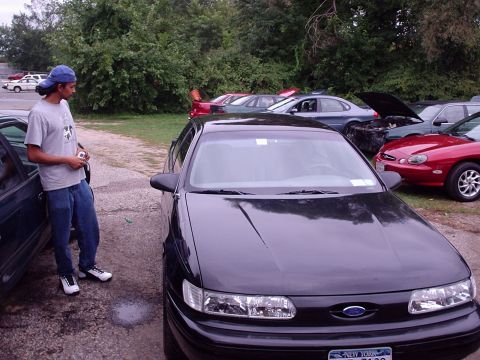 1998 Ford Taurus - A black 1998 Ford Taurus is parked outside with other vehicles in the background.