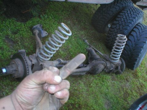 1985 Ford Bronco - Front suspension parts and tires are laid out on the grass, with a hand pointing towards the components.