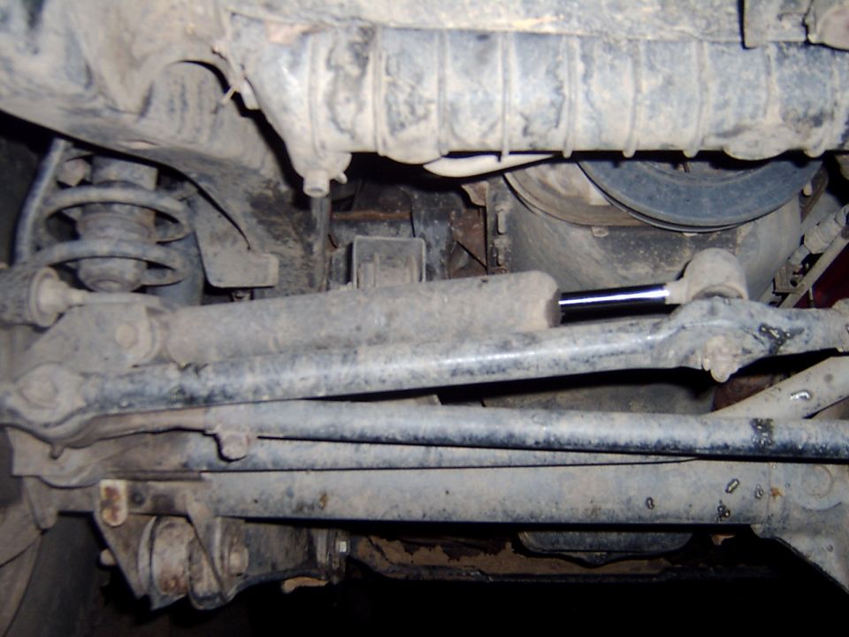 Dusty undercarriage view of tie rod, drag link, coil spring and axle with exhaust above
