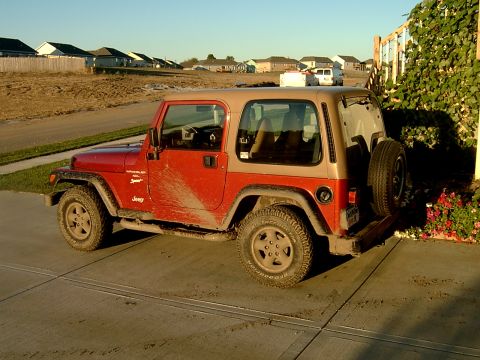 1998 Jeep TJ - A red and tan Jeep Wrangler is parked on a concrete driveway, with a spare tire mounted on the rear.